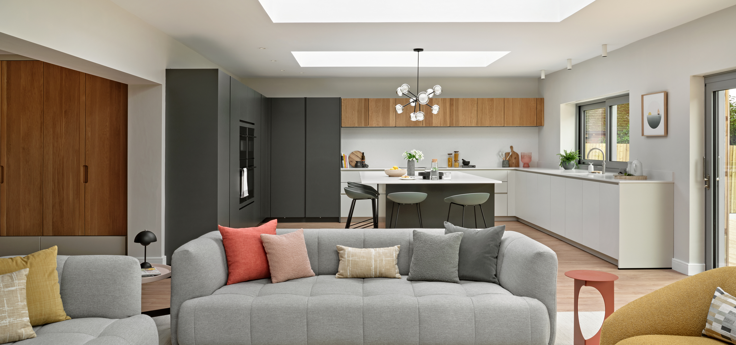 Warm grey sofa in open plan space, with contemporary kitchen in deep green, beige and oak in the background