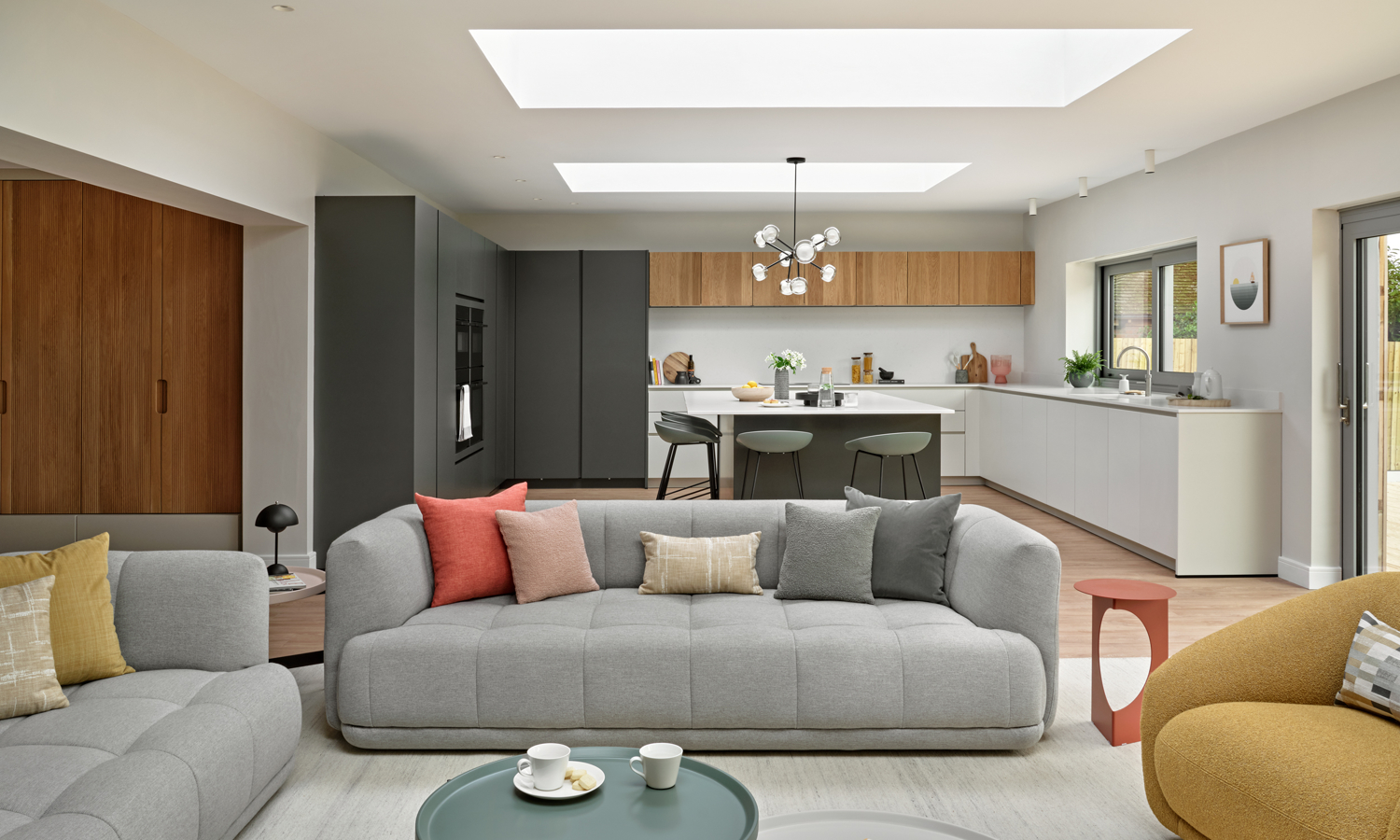 Warm grey sofa in open plan space, with contemporary kitchen in deep green, beige and oak in the background