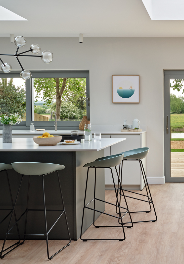 Edge of dark green contemporary kitchen island with green and black modern stools and glass pendant