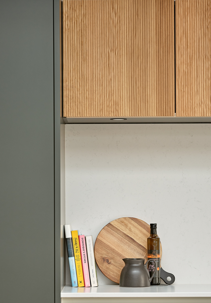Close up showing fluted oak kitchen cupboards with dark green tall cupboard and silestone top