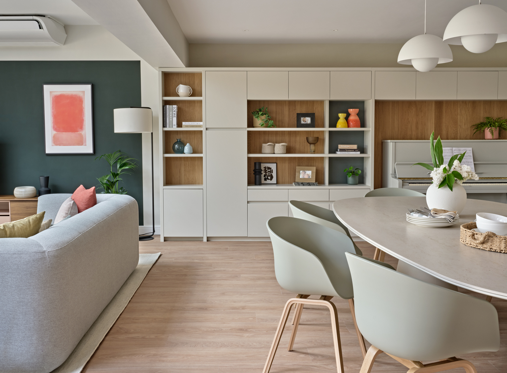 Open plan living space with sofa dining table and bespoke wall unit in neutral tones and deep green