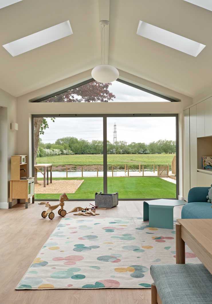 Playroom with contemporary furniture, large rug, view of river through large doors apex window