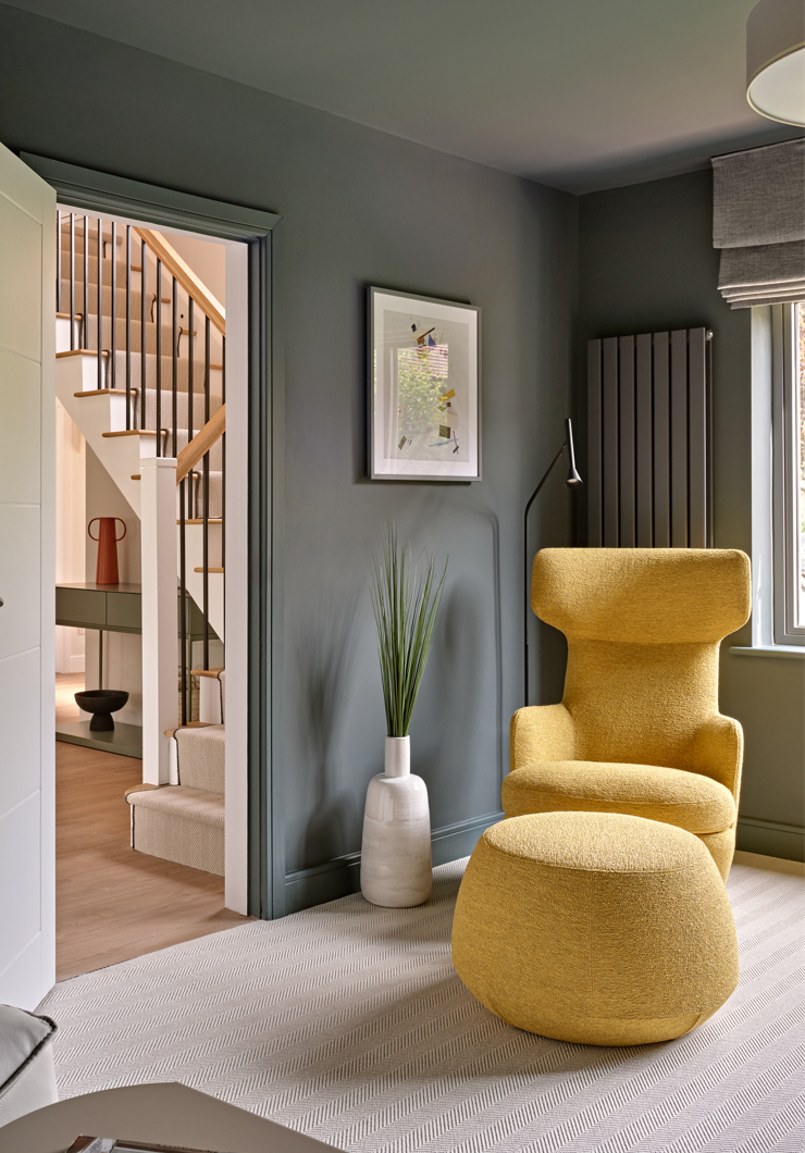 Modern upholstered high back chair with footstool against dark grey wall