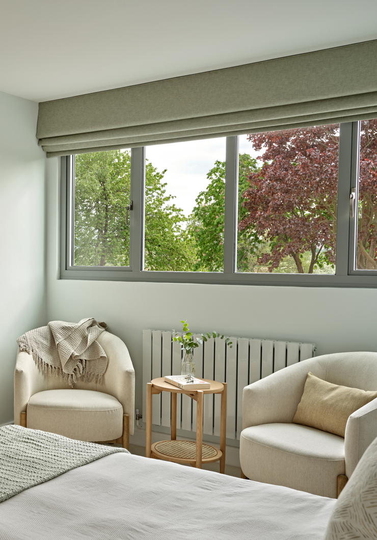 Green and pale blue bedroom with two cream armchairs and side table in oak